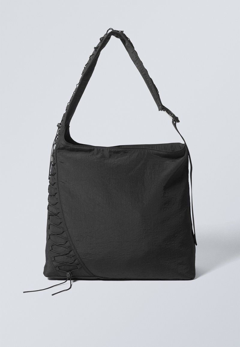 Black fabric tote bag with a textured finish, featuring a wide strap and side lace detailing. Large main compartment with top zipper closure.