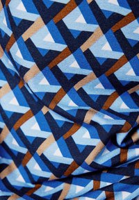Blauer Stoff mit einem geometrischen Muster aus Dreiecken in verschiedenen Blautönen, Braun und Weiß auf einer strukturierten Oberfläche.