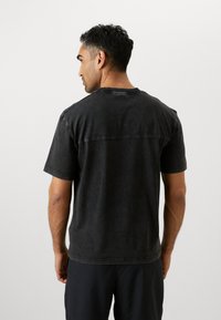 Dunkelgraues Baumwoll-T-Shirt mit kurzen Ärmeln und entspannter Passform. Verfügt über eine horizontale Naht am Rücken und minimale Nähdetails.