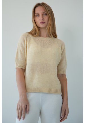 Jasno beżowy sweter z krótkim rękawem, wykonany z miękkiego, puszystego dzianiny, z szerokim dekoltem i ściągaczami przy rękawach. Noszony z kremowymi spodniami o prążkowanej strukturze.