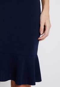 Marinblå figursydd klänning med en utsvängd nederdel. Tillverkad av elastiskt material; slät yta och inga synliga mönster eller accenter.