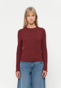 Tummaröd randig långärmad topp med scallopad halsringning och fåll. Matchad med högmidjade blå vida jeans. Slät textur.