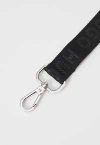 Cinghia in nylon nero con testo embossato, dotata di una clip metallica brillante in argento per attacco, progettata per resistenza e utilità.
