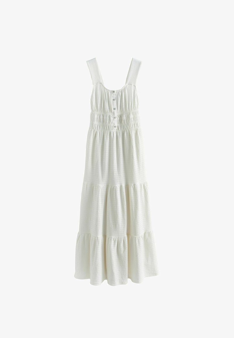 Robe maxi blanche sans manches avec larges bretelles, boutons sur le devant, taille smockée et jupe en tissu texturé à volants.