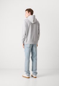 Haut à capuche gris en tissu polaire, doté d'une capuche avec cordons, de poignets et d'une taille côtelés. Assorti à un jean délavé bleu clair et des baskets.