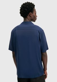 Korte mouwen, marineblauw shirt met een kraag en gladde stof. Bevat een plooi op de rug voor comfort en gemakkelijke beweging.