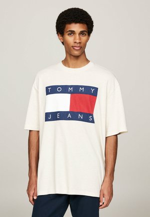 Camiseta de algodón de color crema y corte oversized, con un gráfico en azul marino y rojo que dice "TOMMY JEANS". Manga corta y escote redondo.
