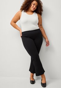 Pantaloni neri a campana con cintura elastica abbinati a una canotta bianca aderente. L'outfit presenta una texture liscia e un design semplice.