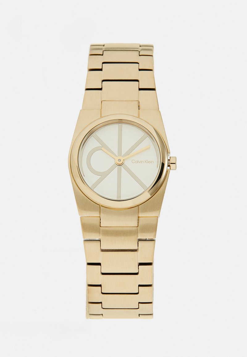 Gold stainless steel watch with a round face, light-colored dial, and geometric pattern. Features a linked bracelet and minimalistic design.