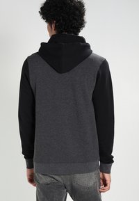 Felpa con cappuccio, cappuccio nero e corpo grigio, caratterizzata da maniche lunghe e polsini a costine. Realizzata in un tessuto morbido e testurizzato.