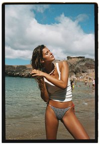 Top bianco senza maniche e parte inferiore del bikini a scacchi con accenti rossi. Ambiente naturale con spiaggia e nuvole sullo sfondo.