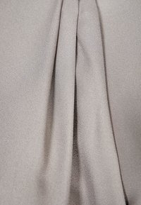 Ljust grått tyg med en texturerad yta och mjuka veck som skapar försiktiga veck. Materialet verkar mjukt och flödande.