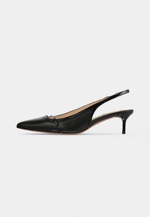 Chaussure slingback pointue en cuir noir avec petit talon kitten et petite bride décorative sur la zone des orteils sur fond uni.