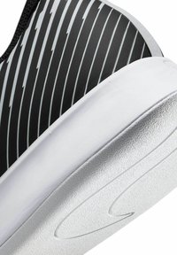 Basket noire avec un dessus texturé, des rayures en forme d'éclair blanches, une semelle lisse blanche et une surface à motif surélevée sur la semelle.