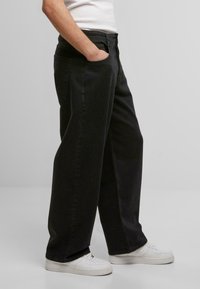 Schwarze weit geschnittene Jeans aus einem Baumwoll-Mischgewebe, mit Seitentaschen und einem regulären Bund, kombiniert mit weißen Sneakers.