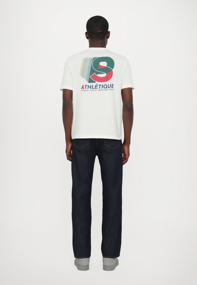 Hvit kortermet t-skjorte med flerfarget grafisk trykk på baksiden. Kombinert med mørkeblå jeans og grå sneakers.