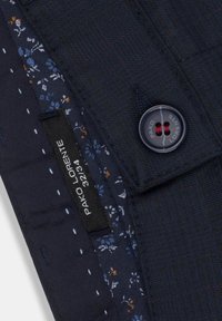 Granatowy materiał o subtelnej, prążkowanej fakturze, z kwiatową podszewką, czarnym guzikiem oraz metką z napisem "Pako Lorente" i rozmiarem.