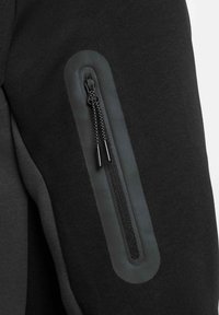 Tejido atlético negro con un bolsillo con cremallera y un panel texturizado en contraste. Suave con un acabado mate, apto para ropa deportiva.