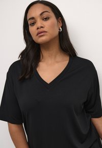 T-shirt noir à col en V avec des manches courtes, fabriqué en tissu doux en mélange de coton. Texture lisse, coupe décontractée, design minimal sans détails supplémentaires.