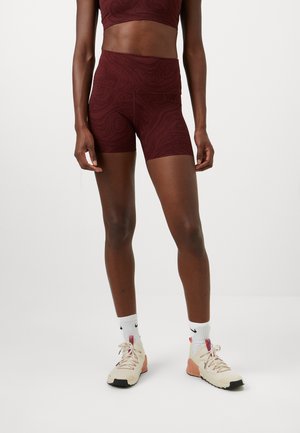 Ensemble de vêtements de sport bordeaux comprenant un haut court et un short taille haute. Texture lisse avec un motif en tourbillon. Chaussures de sport beiges avec des accents roses.