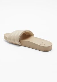 Beige slidesandal med en slät, vadderad rem och platt sula. Har en strukturerad fotsäng och diskret varumärkning på innersulan.