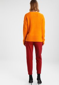 Orange stickad tröja med ribbad fåll, tillsammans med röda slim-fit byxor. Stilettklackar fulländar outfiten.