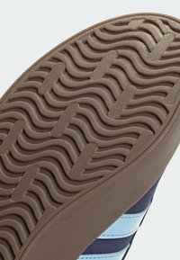 Gummisula med ett bølget mönster. Yttersulan är brun med textur för grepp, designad för dragkraft och hållbarhet.