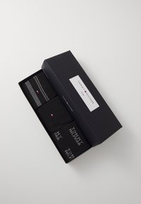 Conjunto de tres pares de calcetines negros almacenados en una caja rectangular negra. Incluye detalles de texto y patrones a rayas, con un logotipo.