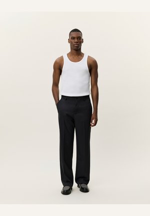 Witte tanktop, zwarte wijde broek en zwarte schoenen. Het materiaal lijkt soepel met een getailleerde silhouet en subtiele details op de schoenen.
