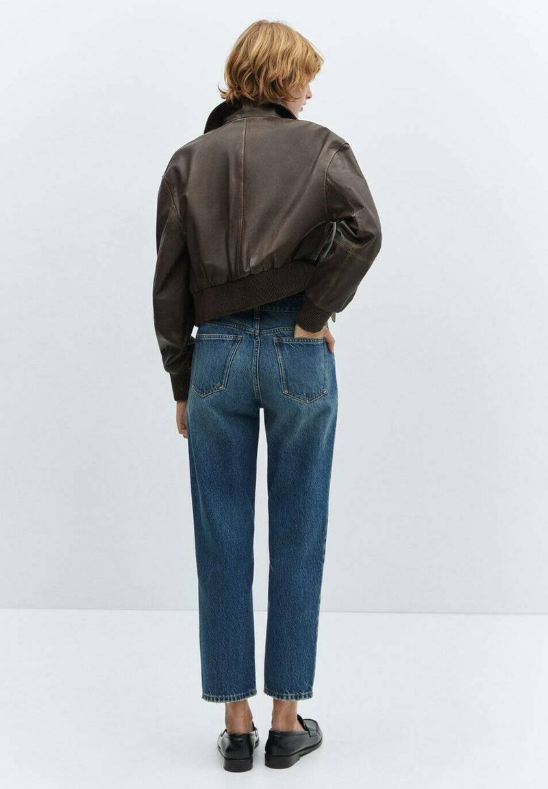 Braune Lederjacke im Crop-Design mit gerippten Bündchen, kombiniert mit hoch taillierten blauen Jeans. Schwarze Schuhe runden das Outfit ab.