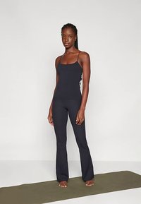 Must sportlik top kitsaste rihmadega, kombineeritud mustade lehvikujuliste retuusidega. Sile tekstuur, keha järgnev lõige, sobib joogaks või treeninguks.