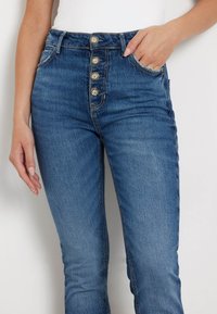 Korkeagaelised sinised denim teksad viie nööbiga kinnitusega, mis sisaldavad esipockets ning slim-fit lõiget. Kangas on kergelt tekstuuriga.