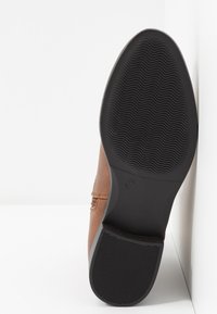 Semelle en cuir marron avec une semelle en caoutchouc noir texturé, présentant un motif ondulé et un marquage de taille 37 sur le talon.