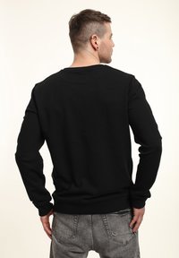 Svart sweatshirt med långa ärmar, rund halsringning, ribbad nederkant och ärmslut, slät textur, bärs med grå jeans, sedd från baksidan.