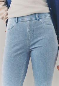 Svetlo modre jeans hlače iz denima s prilagojeno zasnovo, ki vključuje visok pas, sprednje žepe in subtilne šive na šivih.