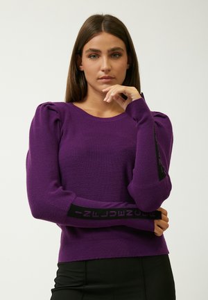 Pull en tricot violet à manches bouffantes, avec une texture côtelée et une bande noire aux poignets avec un texte contrastant.