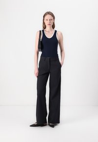 Navy tank top with white trim, paired with black wide-leg trousers. Model holds a black shoulder bag, wearing pointed black flats.