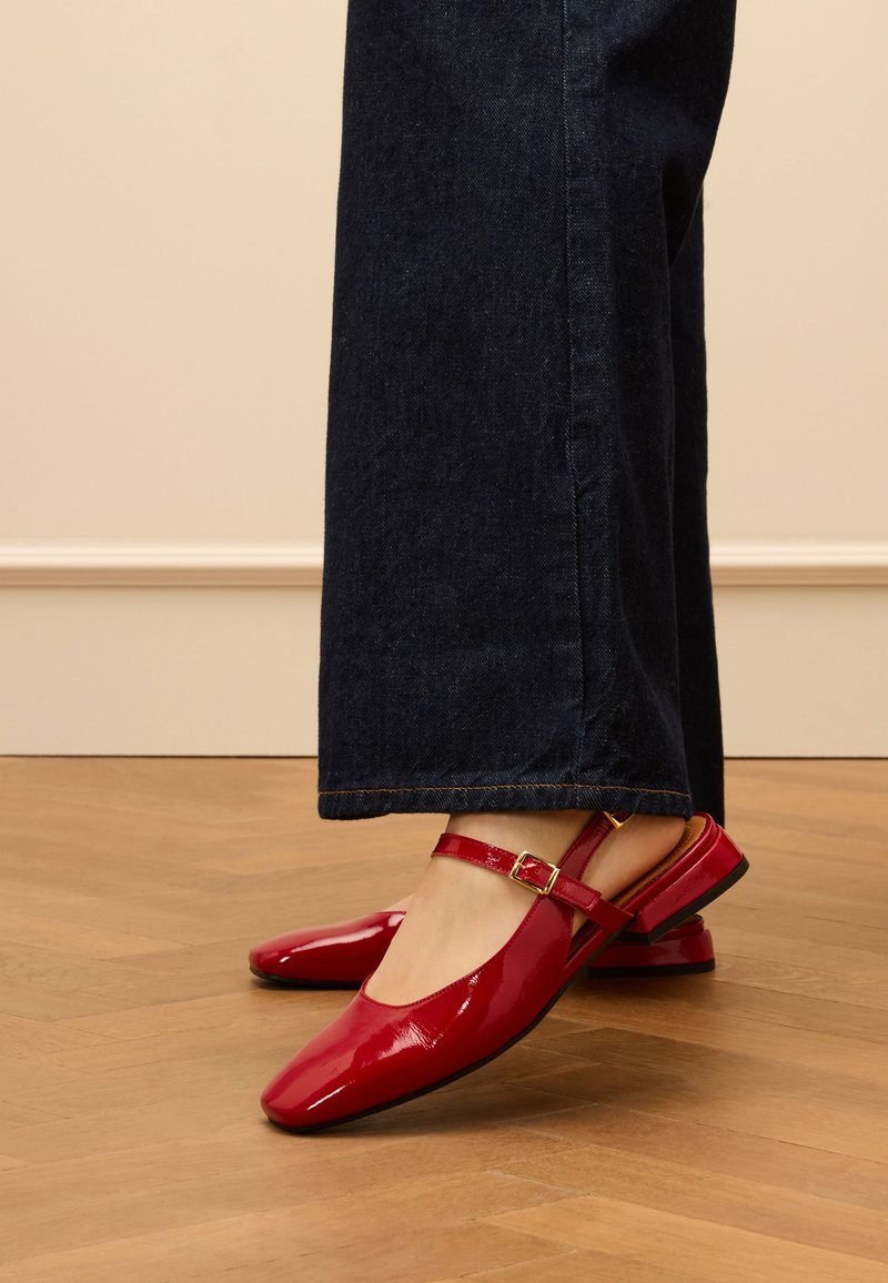 Rode patenten leren slingback schoenen met een vierkante neus, een dunne verstelbare band, en een lage hak, gedragen met donkere spijkerbroek met uitlopende pijpen.