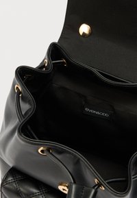 Μαύρη τσάντα από συνθετικό δέρμα με υφή καπιτονέ και χρυσά μεταλλικά στοιχεία, με υφασμάτινη επένδυση και εσωτερική ετικέτα. Σχεδιασμός με ανοιχτή κορυφή για εύκολη πρόσβαση.