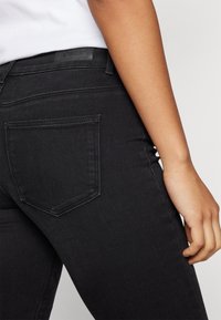 Sorte denim jeans med en tettsittende design, med en baklomme og et lærmerke i livet. Glatt tekstur og klassisk silhuett.