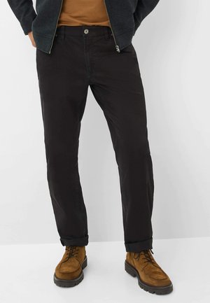 Zwarte katoenen broek met een slim fit, voorzien van een knoopsluiting en opgerolde mouwen, gecombineerd met bruine veterschoenen.