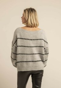 Pull en tricot gris surdimensionné avec des rayures horizontales noires, doté d'une encolure large et d'un ourlet côtelé. Porté avec un pantalon noir ajusté.