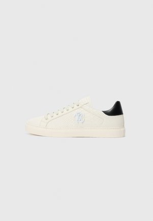 White sneakers featuring a textured upper and smooth black heel accent, round toe, and classic lace-up design. Logo on side panel.