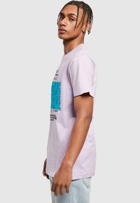 Lys lilla bomulds t-shirt med et grafisk print i blå og sort på fronten. Kortærmede, afslappet pasform og rund halsudskæring.