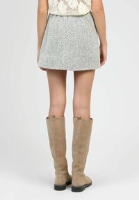 Jupe mini grise texturée avec une taille ajustée et un design évasé, assortie à de grandes bottes en daim beige clair avec une semelle noire.