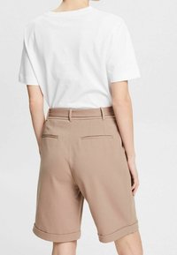 Camiseta blanca de manga corta combinada con pantalones cortos beige de corte ajustado, con dobladillo acampanado y bolsillos traseros sutiles. Textura de tela suave.