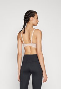 Lys rosa bh med justerbare stropper og baklås, sammen med høyt liv sorte leggings som viser en jevn tekstur.