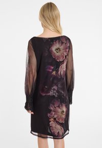 Durchsichtiges schwarzes Kleid mit langen Ärmeln, das mit einem floralen Muster in rosa und lila Tönen gestaltet ist. Enthält Spitzenverzierungen an den Ärmelbündchen.