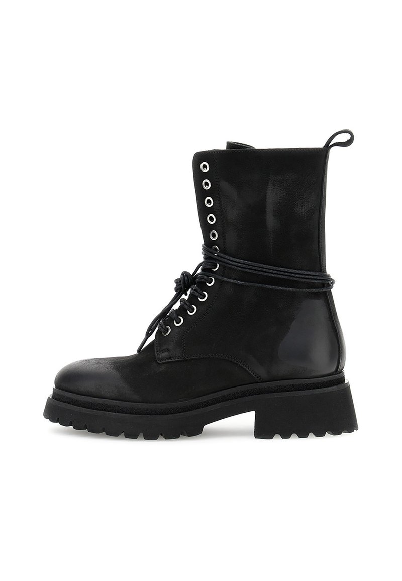 Zwarte combatboot tot halverwege het scheenbeen met dikke profielzool, metalen oogjes, veters om de enkel gebonden en een aantreklabel aan de achterkant.