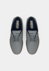 Γκρι καμβά παπούτσια με λείο υφή, διαθέτουν σχέδιο με κορδόνια, καουτσούκ σόλα και λογότυπο "etnies" στην γλώσσα σε ανοιχτό γκρι.